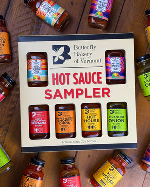 Butterfly Bakery of Vermont hot sauce sampler box with various hot sauce bottles around it on a wooden surface.