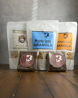 Three packages of granola and two chocolate peanut butter bars with visible brand labels on a wooden surface.