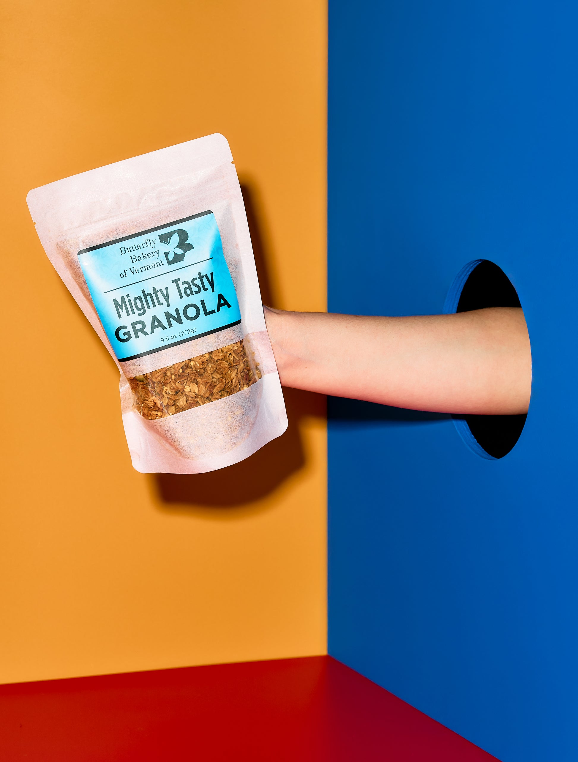 Hand holding a package of 'Mighty Tasty Granola' against a colorful background