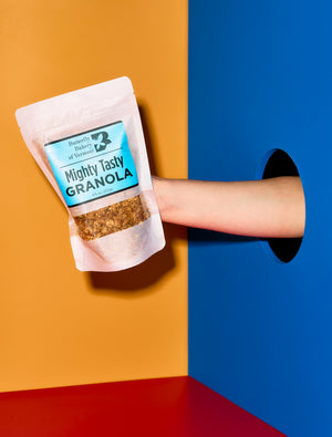 Hand holding a package of 'Mighty Tasty Granola' against a colorful background