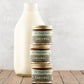 Stacked 2oz jars of Fat Toad Farm Original Caramel Sauce in front of a bottle of milk on a wood surface
