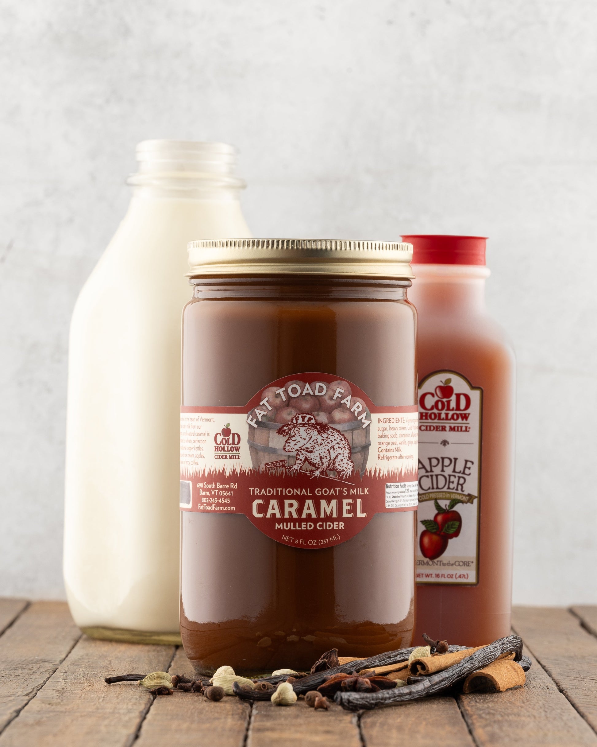 Jar of Fat Toad Farm Mulled Cider caramel in front of a bottle of apple cider and a bottle of milk on a wood table