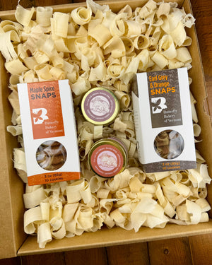 Box containing 2 boxes of Butterfly Bakery of Vermont snaps and 2 jars of Fat Toad Farm caramel, along with decorative wood shavings