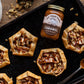 Tarts with apple filling and caramel sauce on a baking tray with a jar of caramel and a spoon.