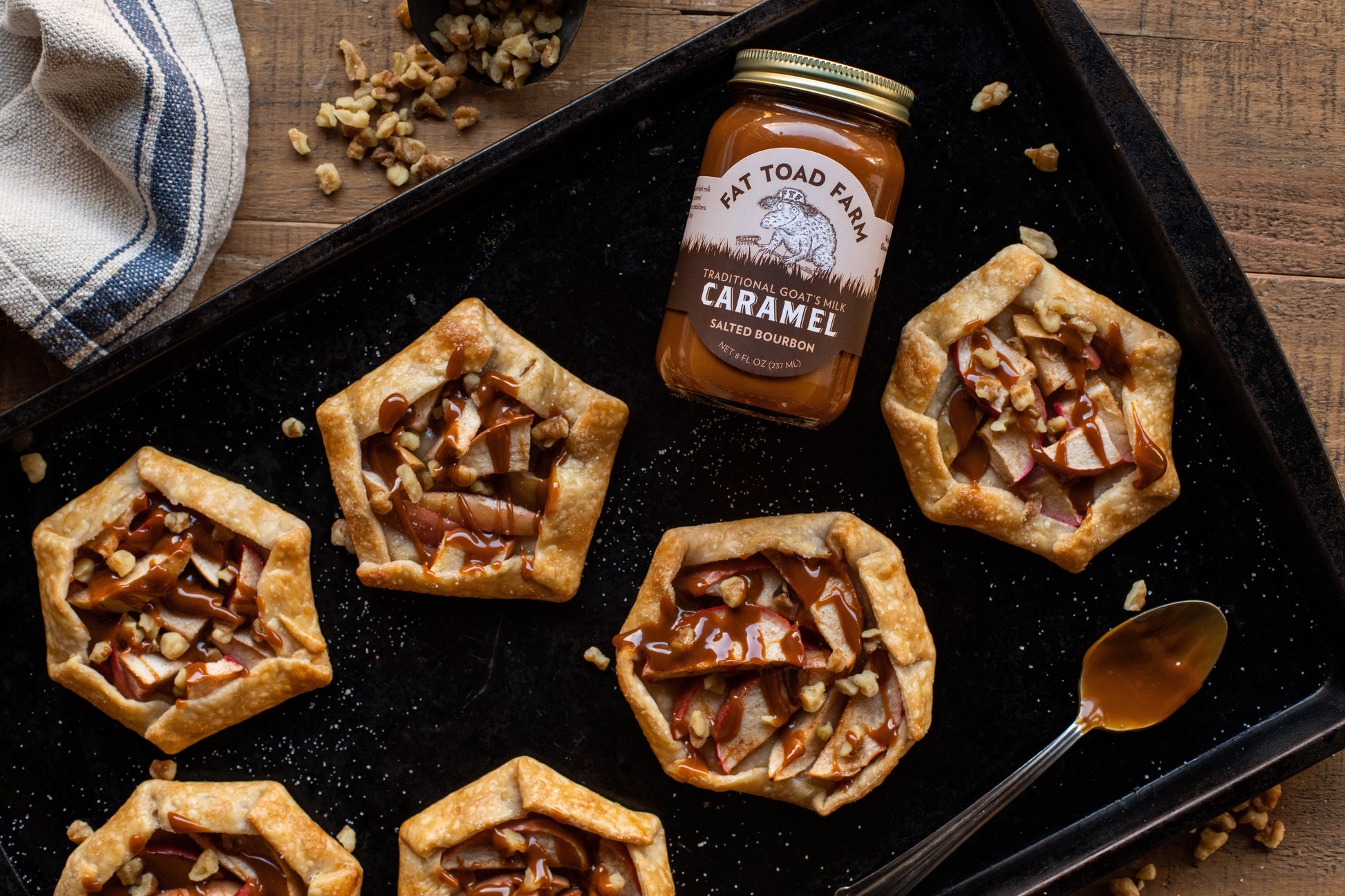 Tarts with apple filling and caramel sauce on a baking tray with a jar of caramel and a spoon.
