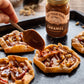 Person drizzling caramel sauce onto small pastries on a baking tray with a jar of Fat Toad Farm Caramel in the background.