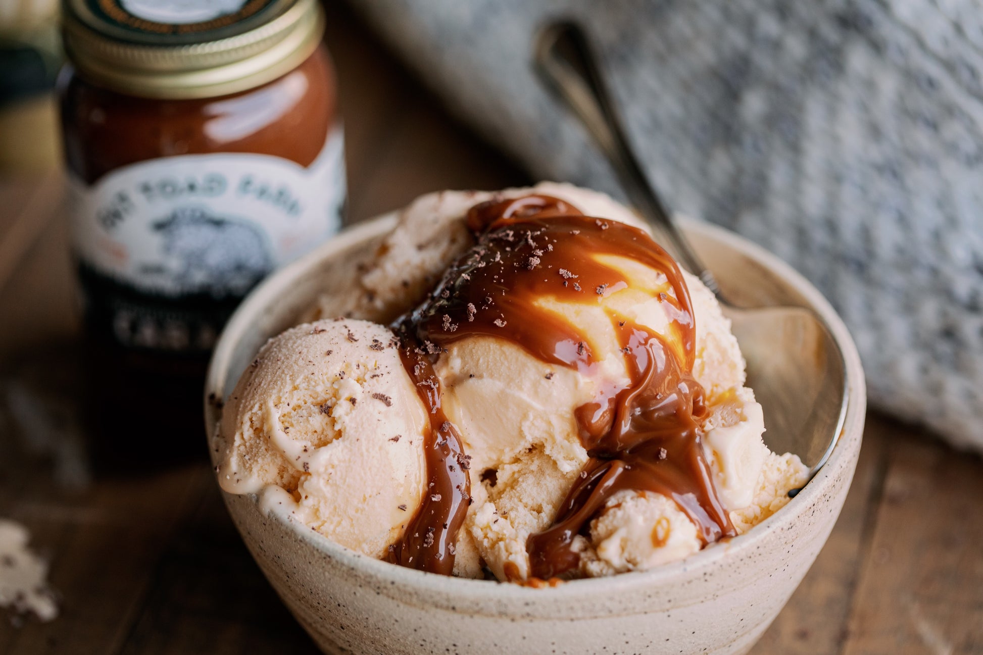 Bowl of ice cream with caramel sauce next to a jar of caramel