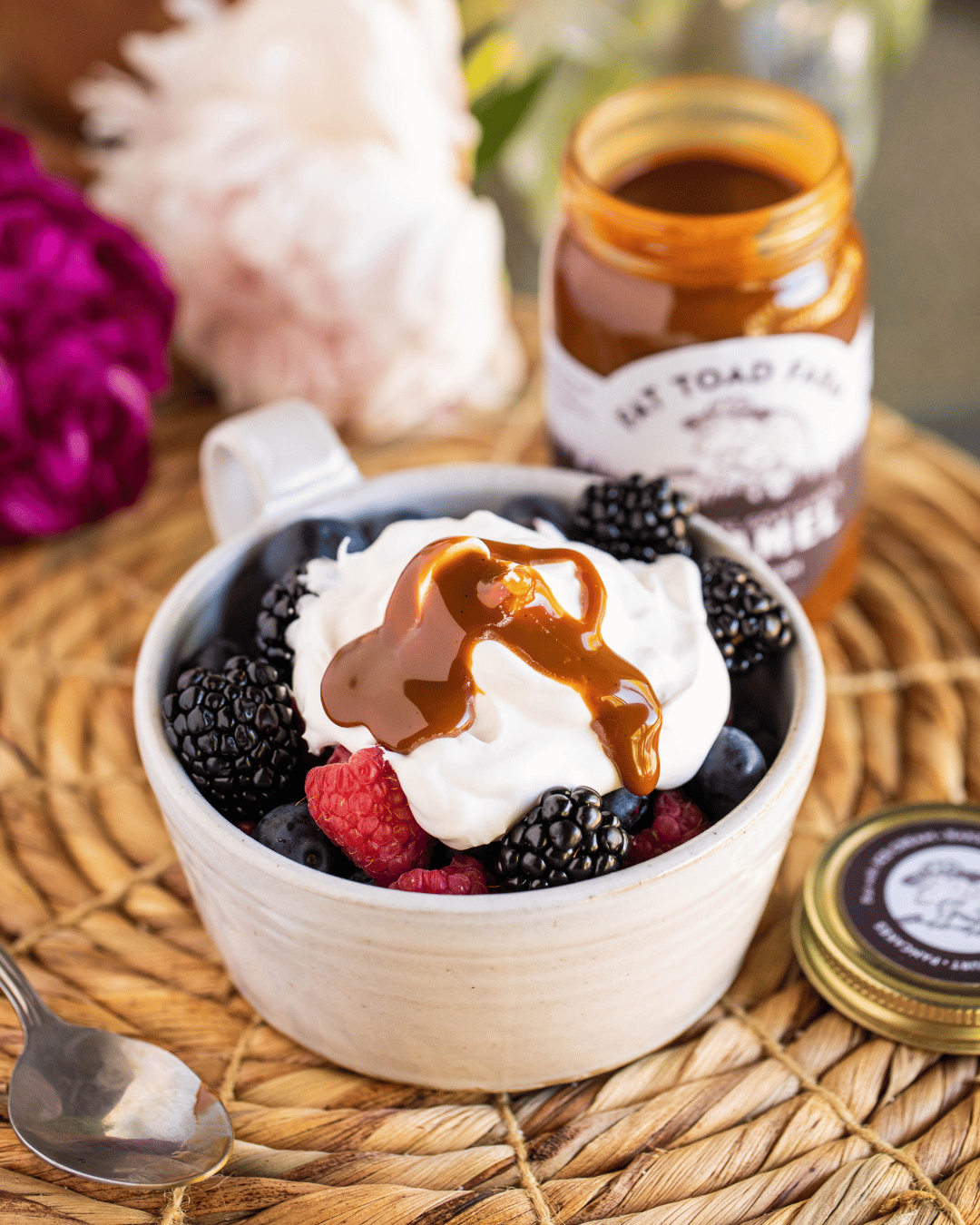 Bowl of dessert with berries and whipped cream, topped with a drizzle of caramel sauce, on a woven mat.