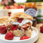 Biscuit with strawberries, cream and caramel on a plate with jars of caramel in the background.