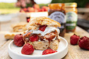 Biscuit with strawberries, cream and caramel on a plate with jars of caramel in the background.