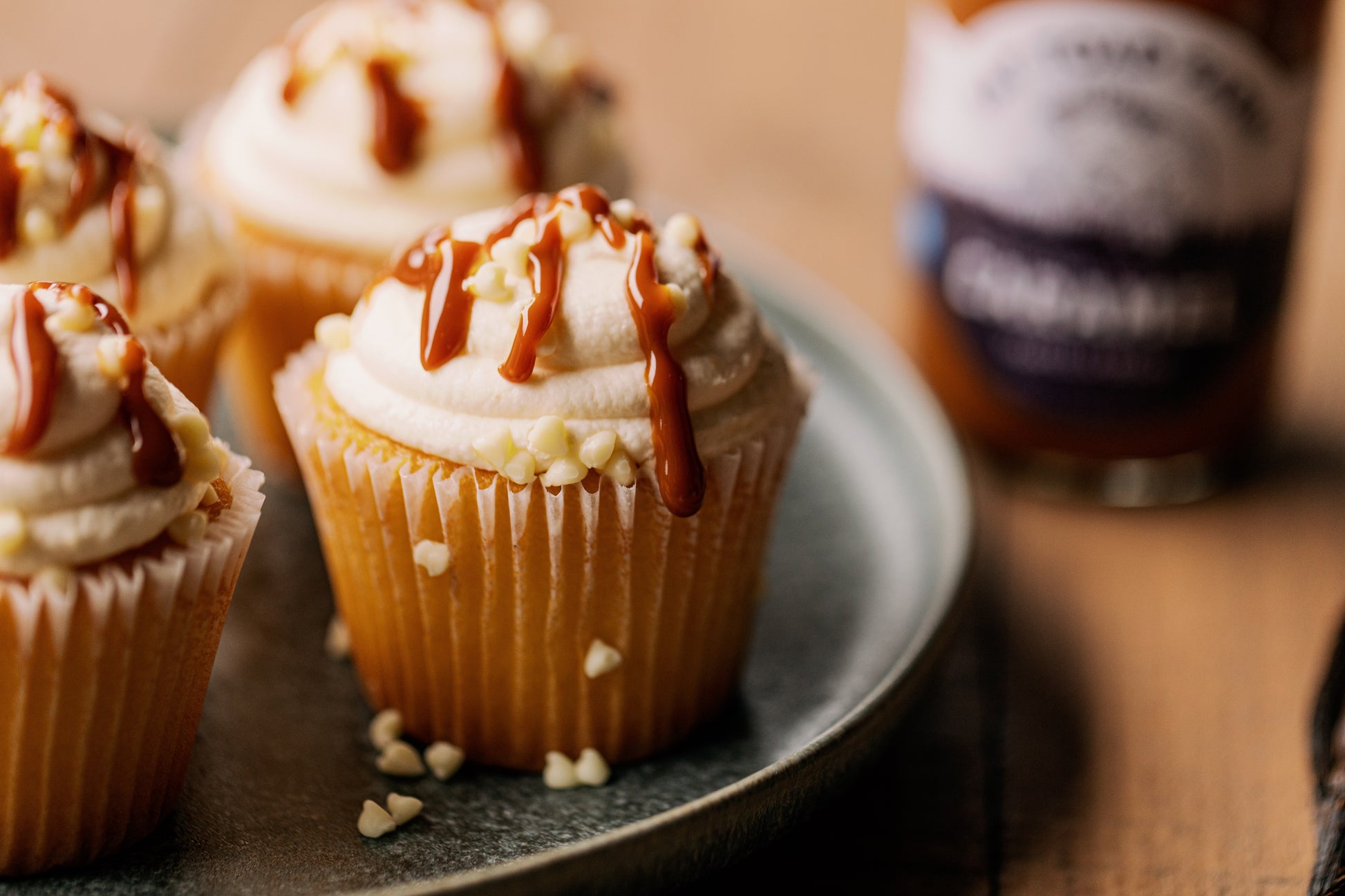 Cupcakes with frosting and caramel sauce on a plate next to a jar of caramel.