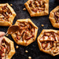 Small apple tarts with caramel sauce on a dark surface, being topped with a spoonful of caramel.
