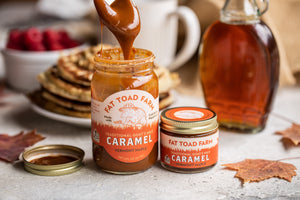 Fat Toad Farm caramel being poured into a jar with a bottle of syrup in the background.