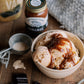Bowl of ice cream with caramel sauce on a wooden surface with a jar of caramel sauce and a container labeled 'French Vanilla Ice Cream'.