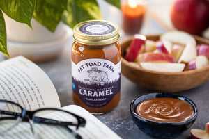 Jar of Fat Toad Farm caramel sauce on a table with apples and a book.