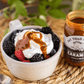 Bowl of berries with whipped cream and caramel sauce next to a jar of Fat Toad Farm caramel.