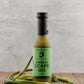 Bottle of Garlic Scape Sauce from Butterfly Bakery of Vermont on a wooden surface with garlic scapes.