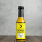 Bottle of Dutchess Mystery Pepper hot sauce on a wooden surface with a gray background