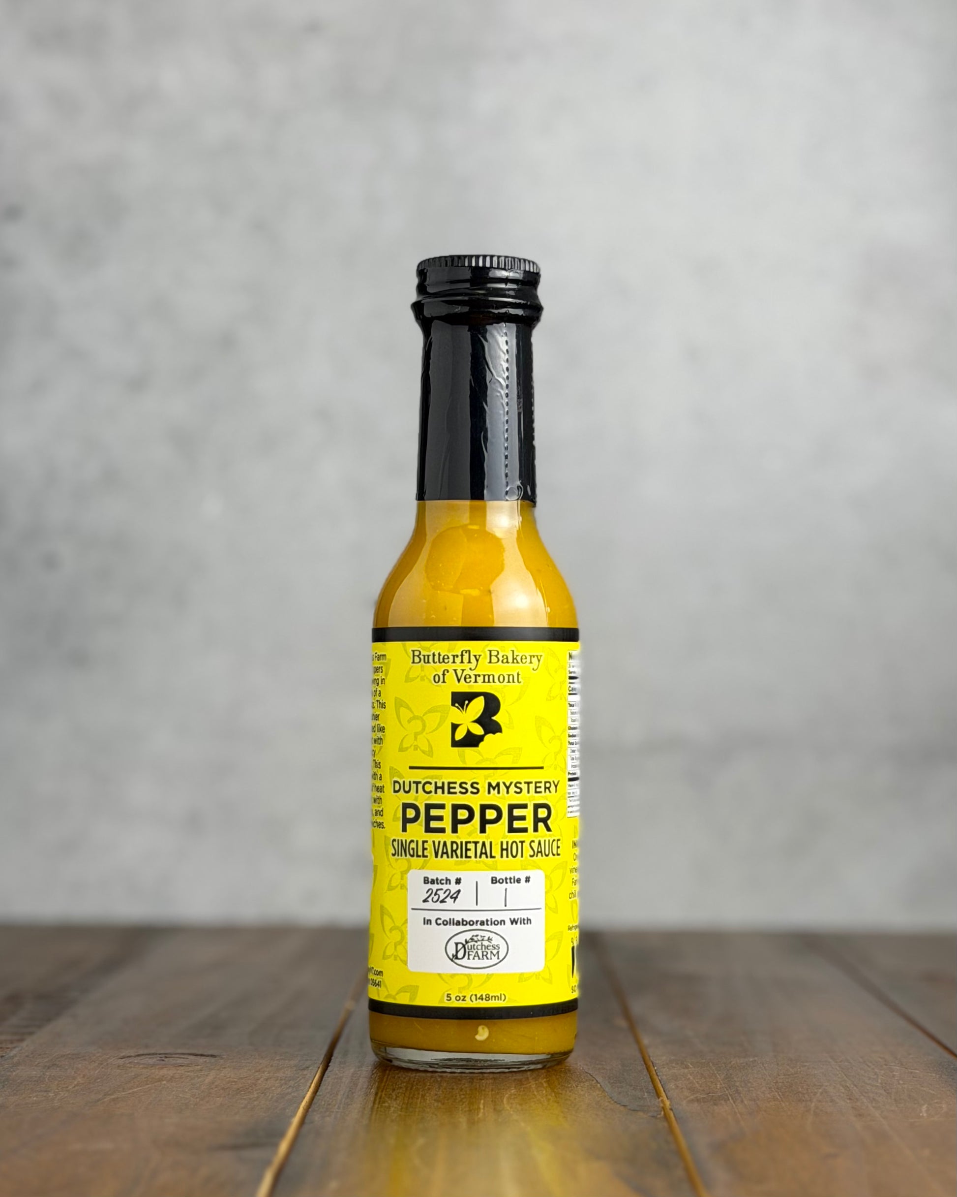 Bottle of Dutchess Mystery Pepper hot sauce on a wooden surface with a gray background