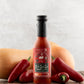 Bottle of Butterfly Bakery of Vermont Ooh La La Hot Sauce on a wood surface with red jalapenos and a butternut squash in the background.