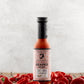 Bottle of Butterfly Bakery of Vermont Red Ghost Reaper Hot Sauce surrounded by red ghost peppers on a wooden surface