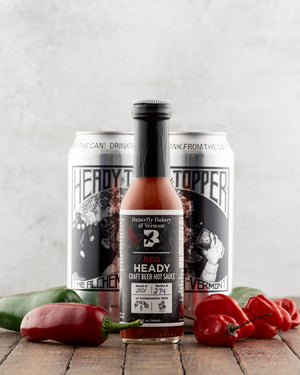 Bottle of Butterfly Bakery of Vermont Red Heady Hot Sauce next to cans of Heady Topper beer, jalapenos and ghost peppers