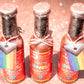 Three bottles of Maple Sparkle Sriracha Pride Hot Sauce from Butterfly Bakery of Vermont on a table being dusted with glitter from above