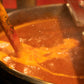 Red hot sauce in a giant kettle with edible glitter being stirred into it