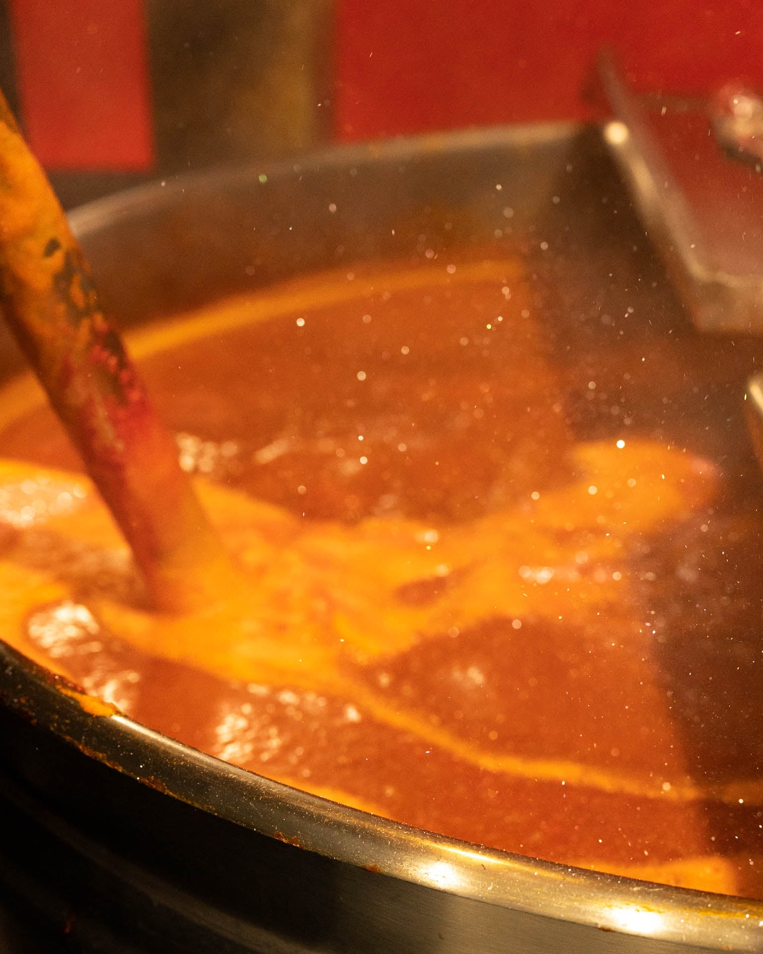 Red hot sauce in a giant kettle with edible glitter being stirred into it