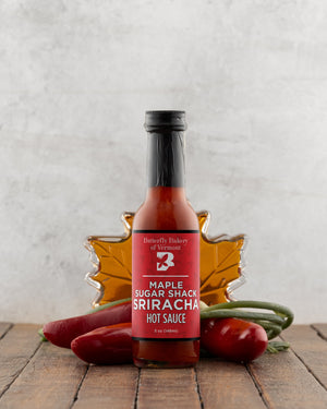 Bottle of Maple Sugar Shack Sriracha Hot Sauce with decorative elements on a wooden surface