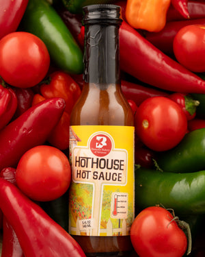 Bottle of Hot House Hot Sauce from Butterfly Bakery of Vermont lying on a bed of hot peppers and tomatoes