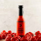 Bottle of Vermont Habs hot sauce surrounded by red peppers on a wooden surface.
