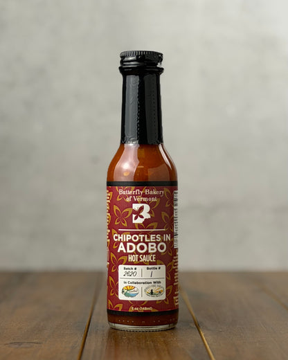 Bottle of Chipotles In Adobo hot sauce from Butterfly Bakery of Vermont on a wooden tabletop