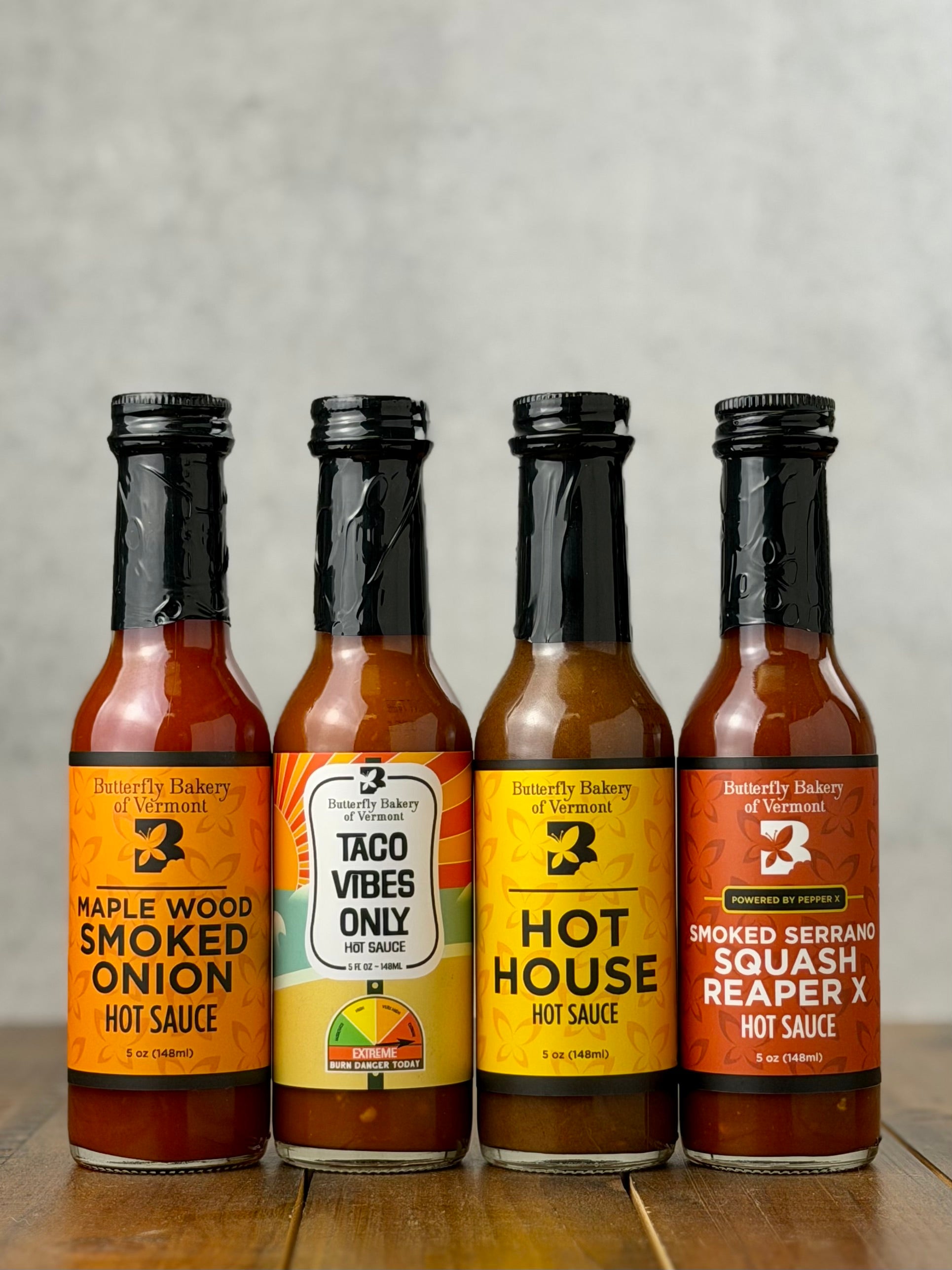 Bottles of all four hot sauces from Butterfly Bakery of Vermont that have appeared on Hot Ones, all on a wooden surface