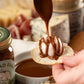 Person drizzling caramel onto a cracker topped with goat cheese with various crackers and cheese in the background.