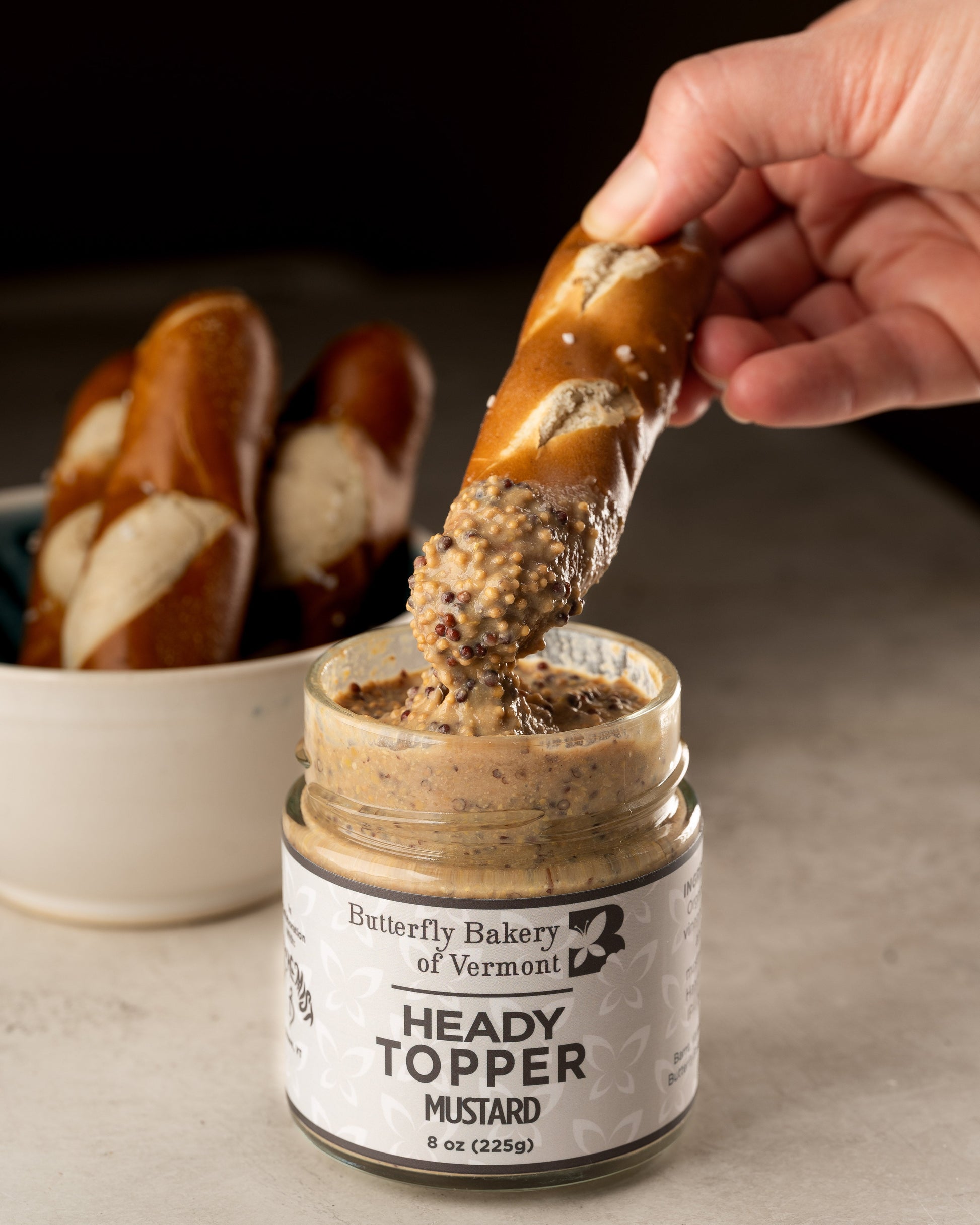 Someone dipping a soft pretzel stick into a jar of Heady Topper mustard from Butterfly Bakery of Vermont