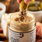 Hand dipping a pickle into a jar of Heady Topper Mustard with a blurred background