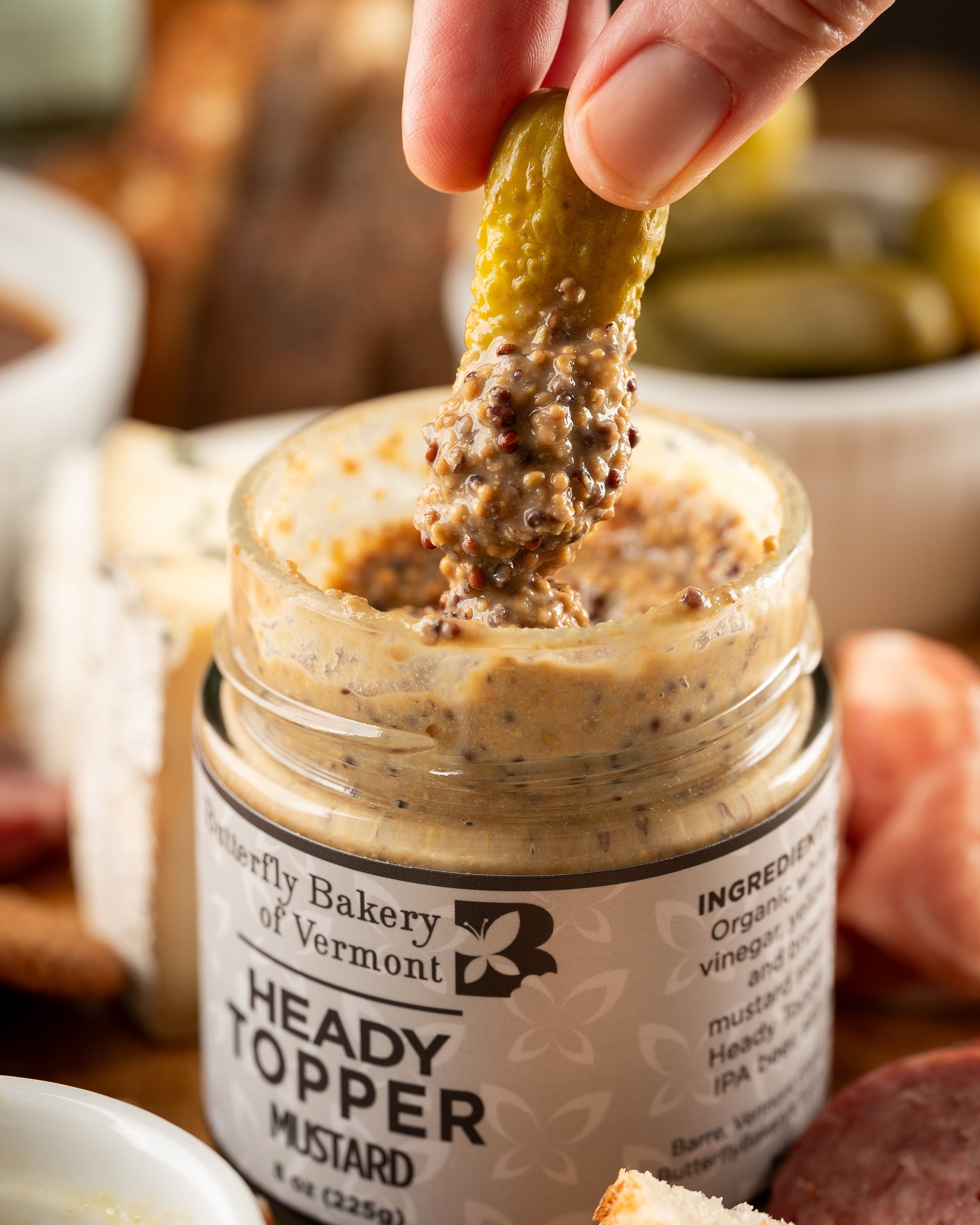 Hand dipping a pickle into a jar of Heady Topper Mustard with a blurred background