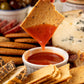 Hand dipping a cracker into a small bowl of hot sauce with a platter of crackers and cheese in the background.