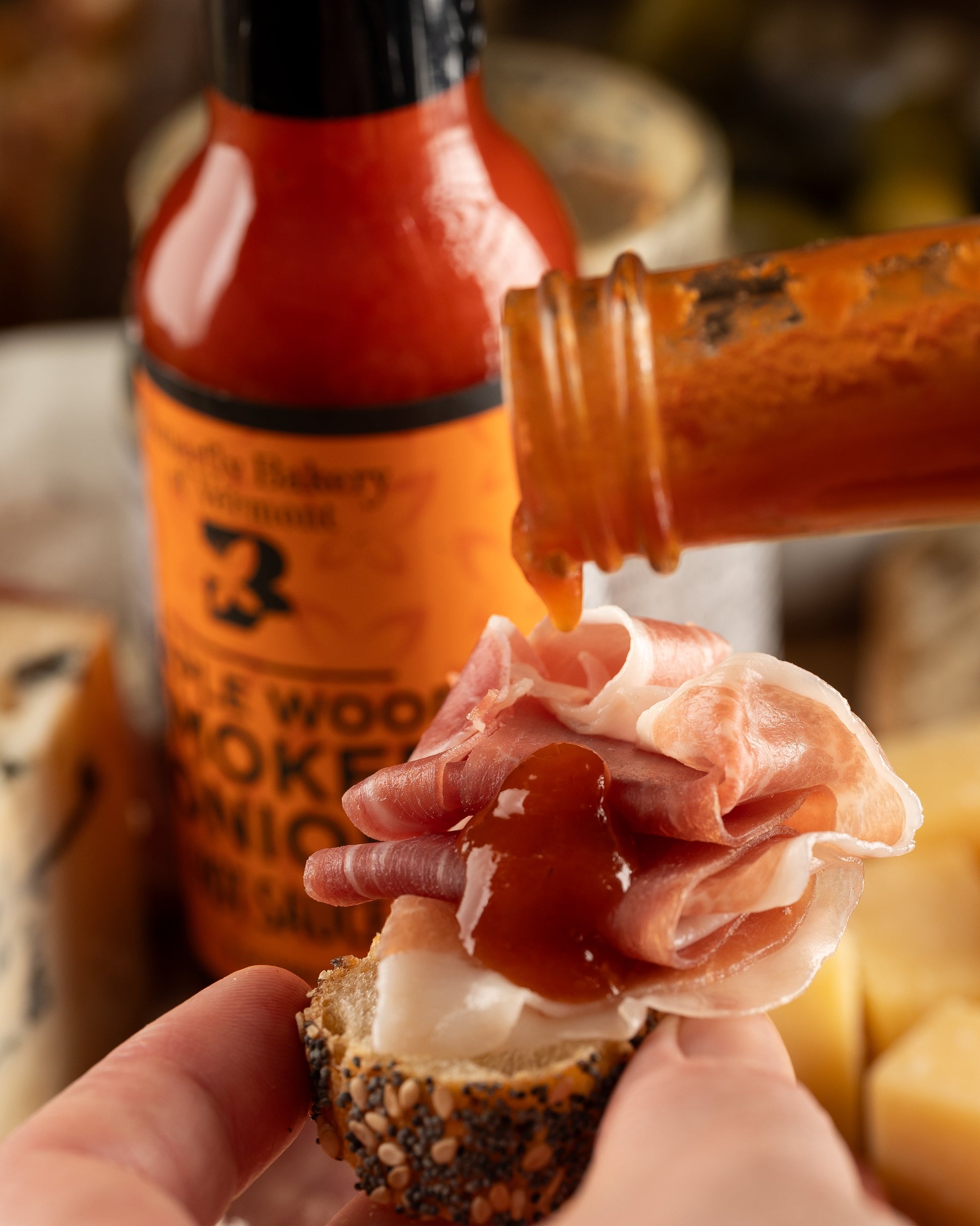 Hot sauce being poured onto a slice of bread with cheese and ham, with a bottle of hot sauce in the background.