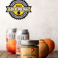 Jar of Butterfly Bakery of Vermont Hard Cider Smoked Onion Mustard with a gold metal badge sitting on a wood surface with 2 cans of hard cider, an onion and 2 apples
