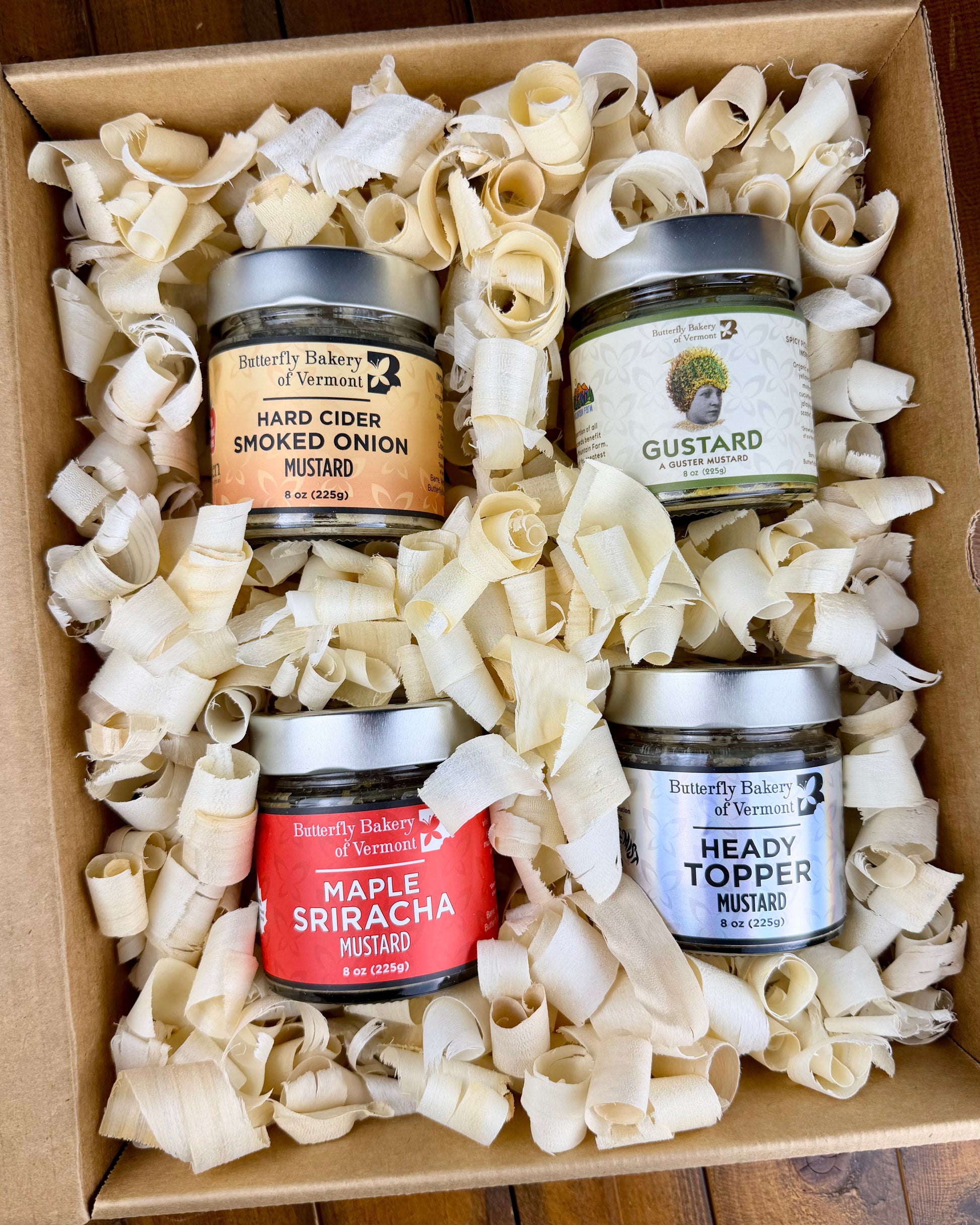 Four jars of Butterfly Bakery of Vermont mustard in a box with decorative wood shavings