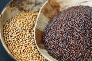 Two wooden bowls containing different types of mustard seeds