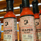 Bottles of Red Ghost Reaper hot sauce on a wooden surface