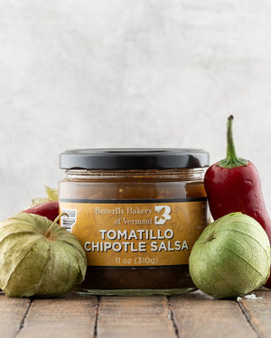 Butterfly Bakery of Vermont Tomatillo Chipotle Salsa on a wood surface with red peppers and tomatillos