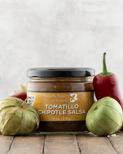 Butterfly Bakery of Vermont Tomatillo Chipotle Salsa on a wood surface with red peppers and tomatillos