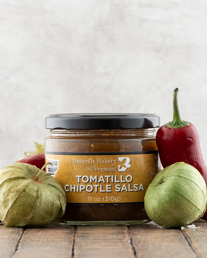 Butterfly Bakery of Vermont Tomatillo Chipotle Salsa on a wood surface with red peppers and tomatillos