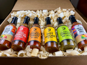 Six bottles of Butterfly Bakery of Vermont hot sauce in a box with decorative wood shavings
