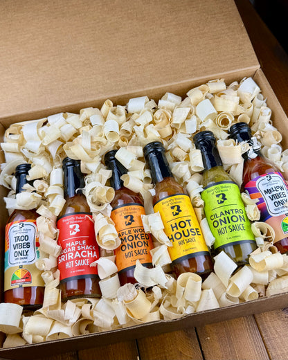Six bottles of Butterfly Bakery of Vermont hot sauce in a box with decorative wood shavings