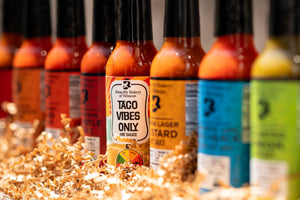 Row of hot sauce bottles with visible labels on a textured surface